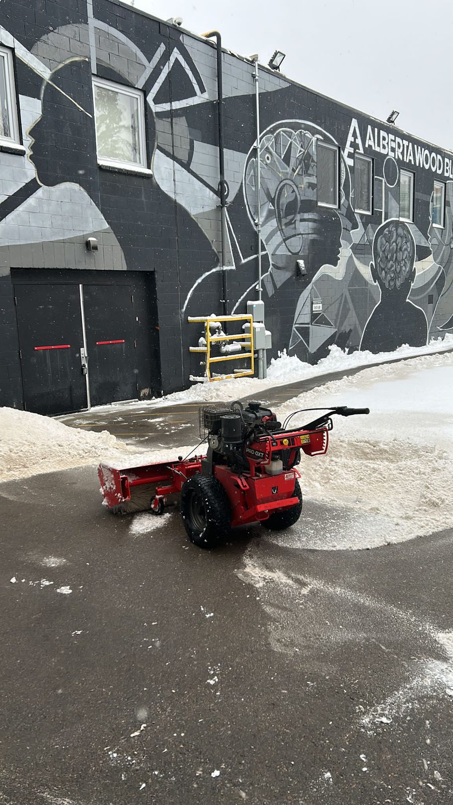 Walk-behind snow machine clearing a commercial lot in Calgary during a snowfall